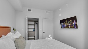 A hotel room with a bed, a wardrobe, a mirror, a picture of a cityscape, and a door. - The Crosby Miami Worldcenter (Miami)