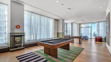 A modern living room with a pool table, large windows, and a seating area.