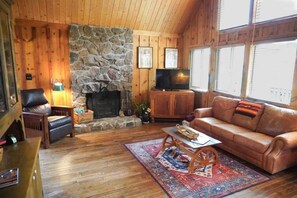 Ein gemütliches Blockhäuschen-Interieur mit Kamin aus Stein, Ledersofa und Fernseher.