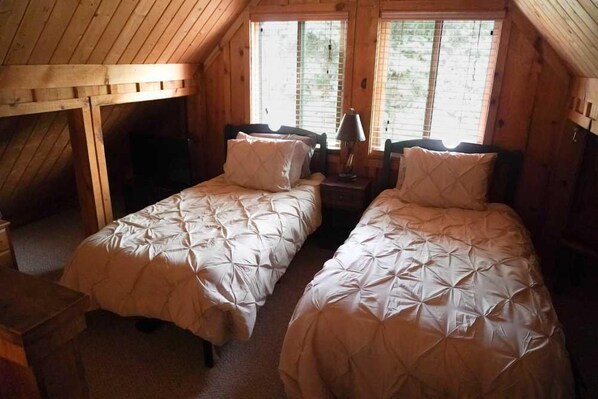 A room with two beds, each with a matching headboard and pillow, and a small table with a lamp.