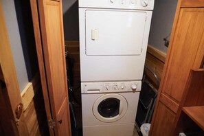 A compact laundry room with a stacked washer and dryer, wooden cabinets, and a visible electrical outlet.