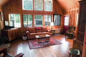 Ein gemütliches Blockhaus-Interieur mit Holzbalkendecke, Ledersofa, Couchtisch und einem gemusterten Teppich.