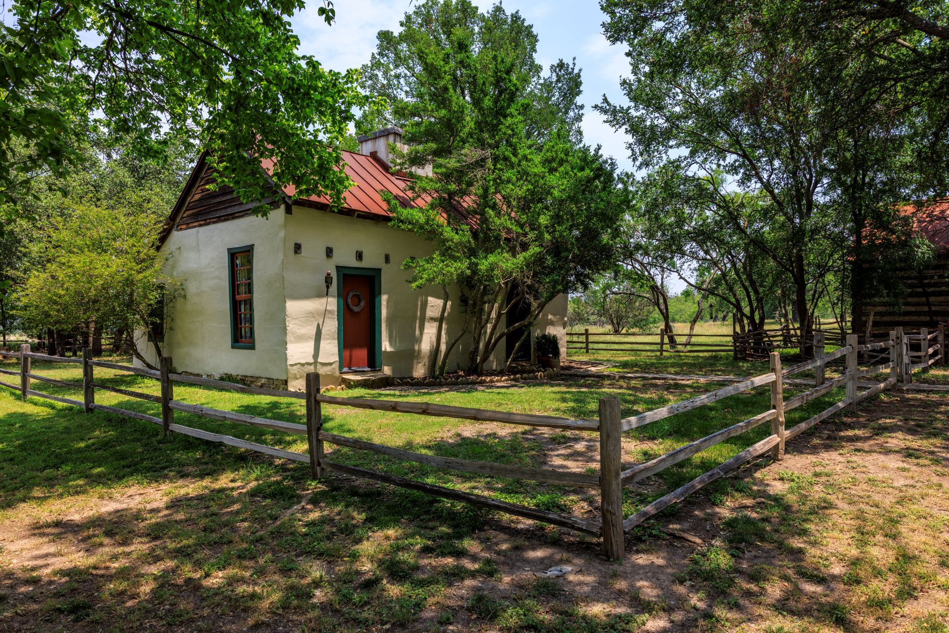 A rustic building with a red door, surrounded by a wooden fence and trees.