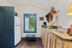A compact kitchen with a white refrigerator, a window with blue trim, a wooden bench, and a sink with various kitchen items. - An 1849 farmhouse that traveled 1,200 miles (Fredericksburg)