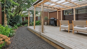 A wooden deck with a pergola, a grill, and a wicker chair.