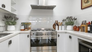 A kitchen with white cabinetry, a stainless steel stove, and potted plants on the countertops.