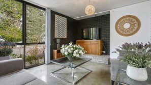 Una sala de estar moderna con una mesa de centro de vidrio, un mueble de madera y un televisor frente a una pared de ladrillo negro.