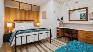 A hotel room with a bed, bedside tables, a desk, a chair, a dresser, and a mirror.