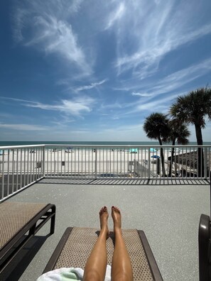A beach view with a metal railing, a bench, and a person lying on the ground. - Oceanfront Paradise in Madeira Beach. Private Balcony. Pool & Hot Tub (Madeira Beach)