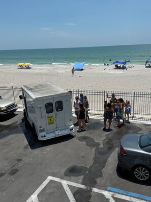 Eine Strandansicht mit einem weißen Van, der am Straßenrand geparkt ist, einem Auto und Menschen, die sich am Wasser versammelt haben.