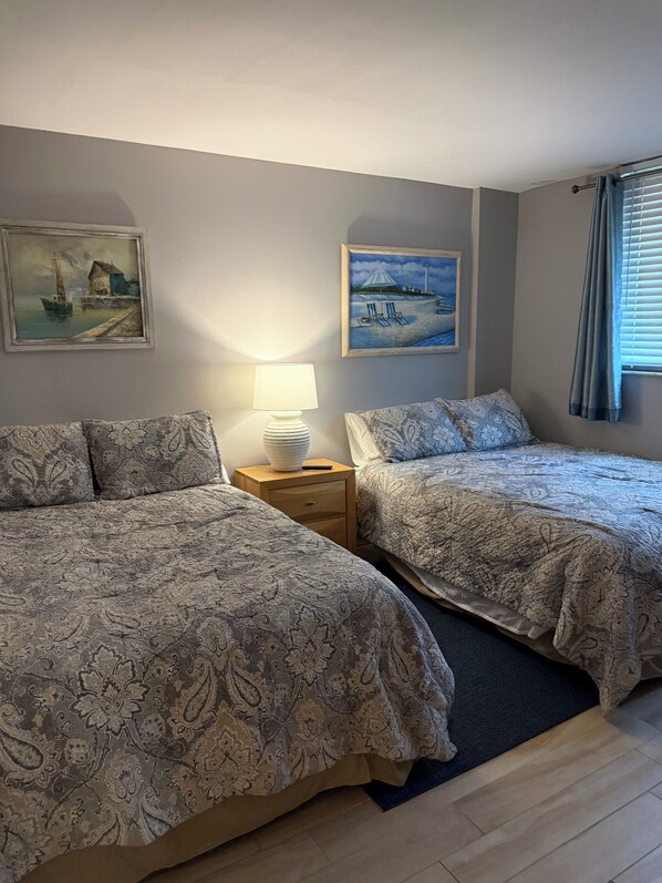A hotel room with two beds, a nightstand with a lamp, and two paintings on the wall. - Oceanfront Paradise in Madeira Beach. Private Balcony. Pool & Hot Tub (Madeira Beach)