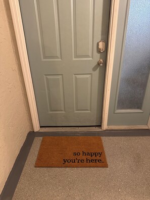 A door with a doormat that reads 'so happy you're here.' - Oceanfront Paradise in Madeira Beach. Private Balcony. Pool & Hot Tub (Madeira Beach)