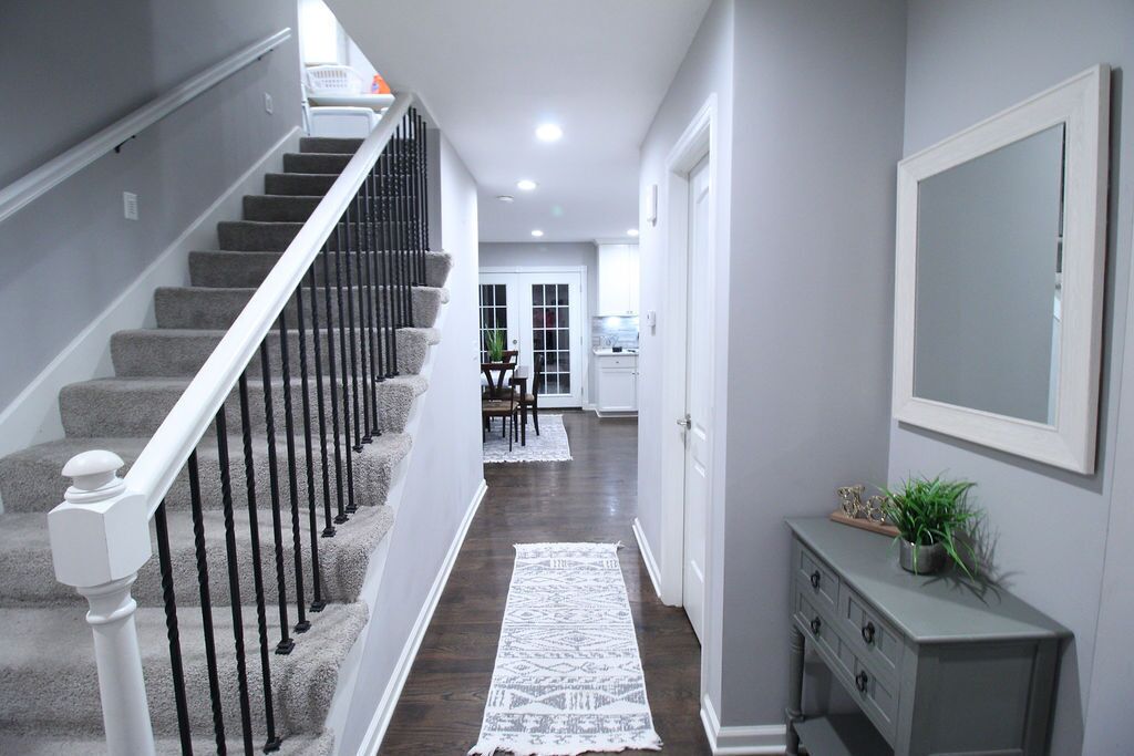 A hallway with a staircase, a white console table with a plant, and a large mirror on the wall.