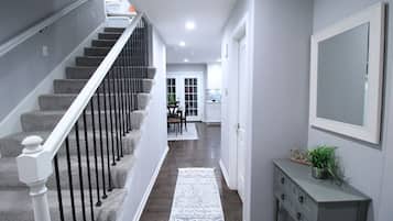 A hallway with a staircase, a white console table with a plant, and a large mirror on the wall.