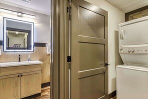 A hotel room with a wooden vanity, a mirror, a towel rack, and a front-loading washer and dryer. - Bear Trap in the Glades (Gatlinburg)