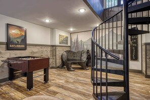 Ein Zimmer mit einem Kicker, einer Bärenstatue und einer Treppe mit Metallgeländer.