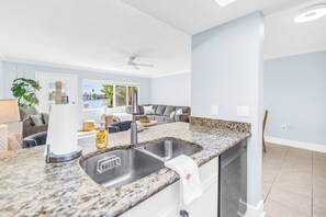 A modern kitchen with a granite countertop, a built-in sink, and a ceiling fan. - NEW! Flamingo Breeze Waterfront • Walk to Beach and Restaurants (Treasure Island)