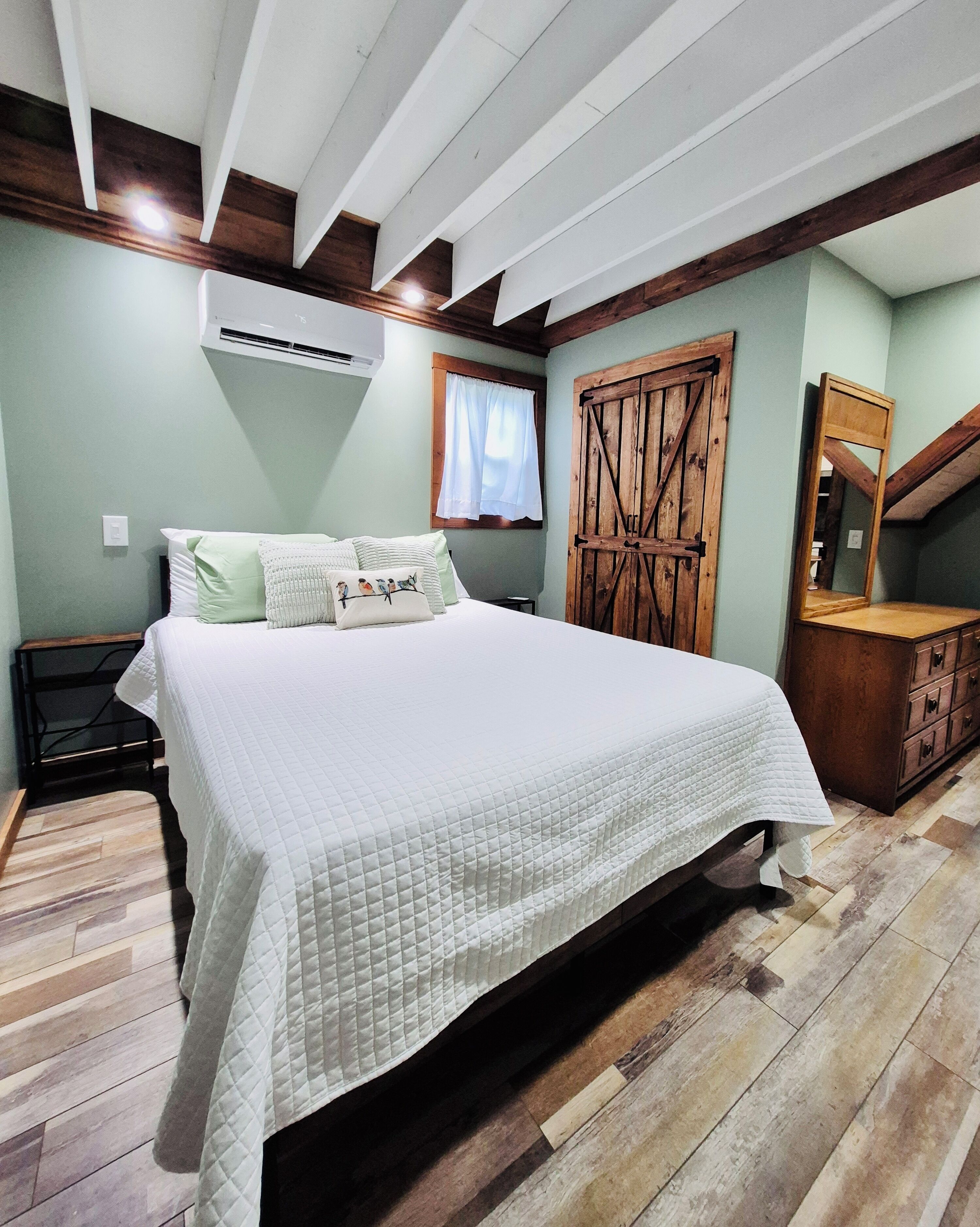 Une chambre à coucher comprenant un lit, une armoire en bois, un miroir et un appareil de climatisation.
