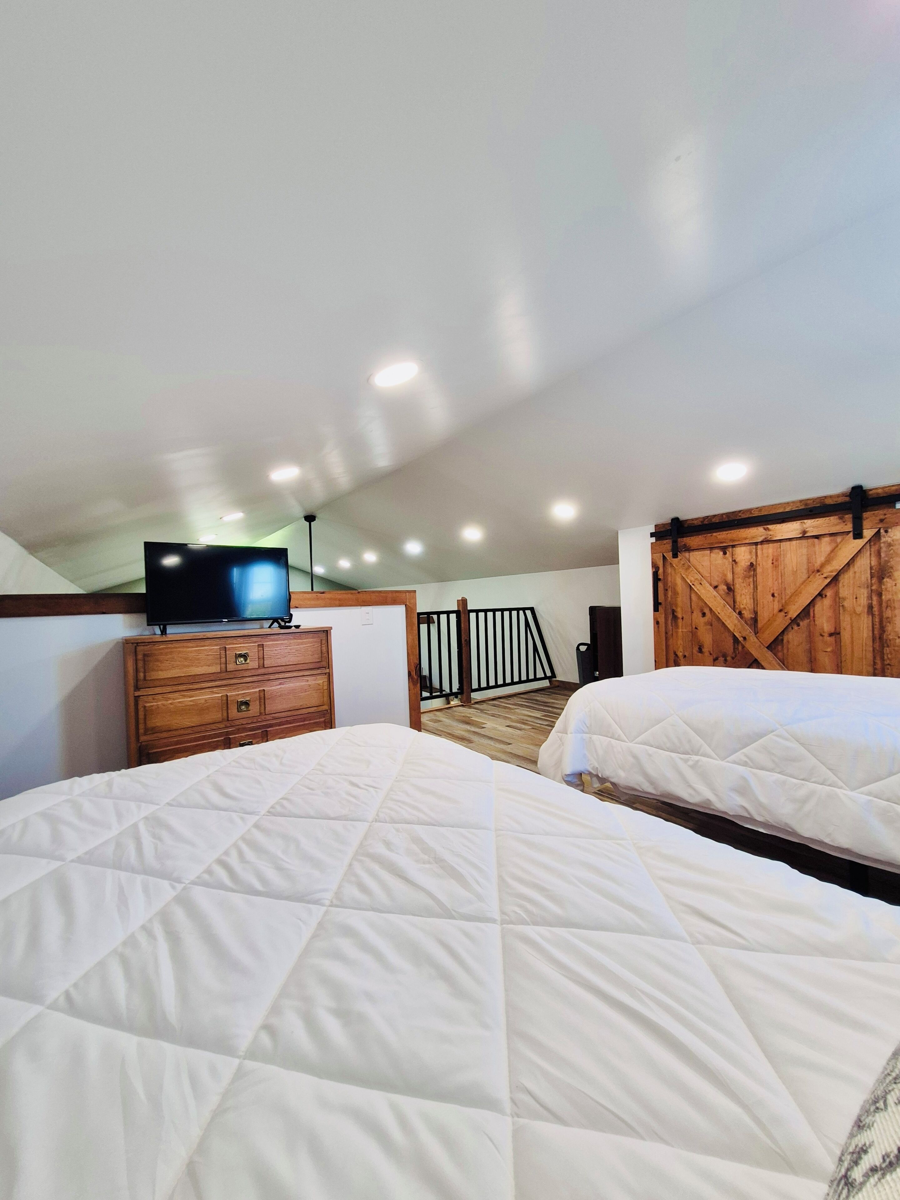 Une chambre avec deux lits, une commode en bois, un téléviseur et un mur en bois de style grange.