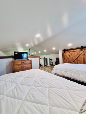 Une chambre avec deux lits, une commode en bois, un téléviseur et un mur en bois de style grange.