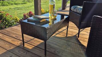 A wooden deck with a glass table, a bottle of wine, and a book.