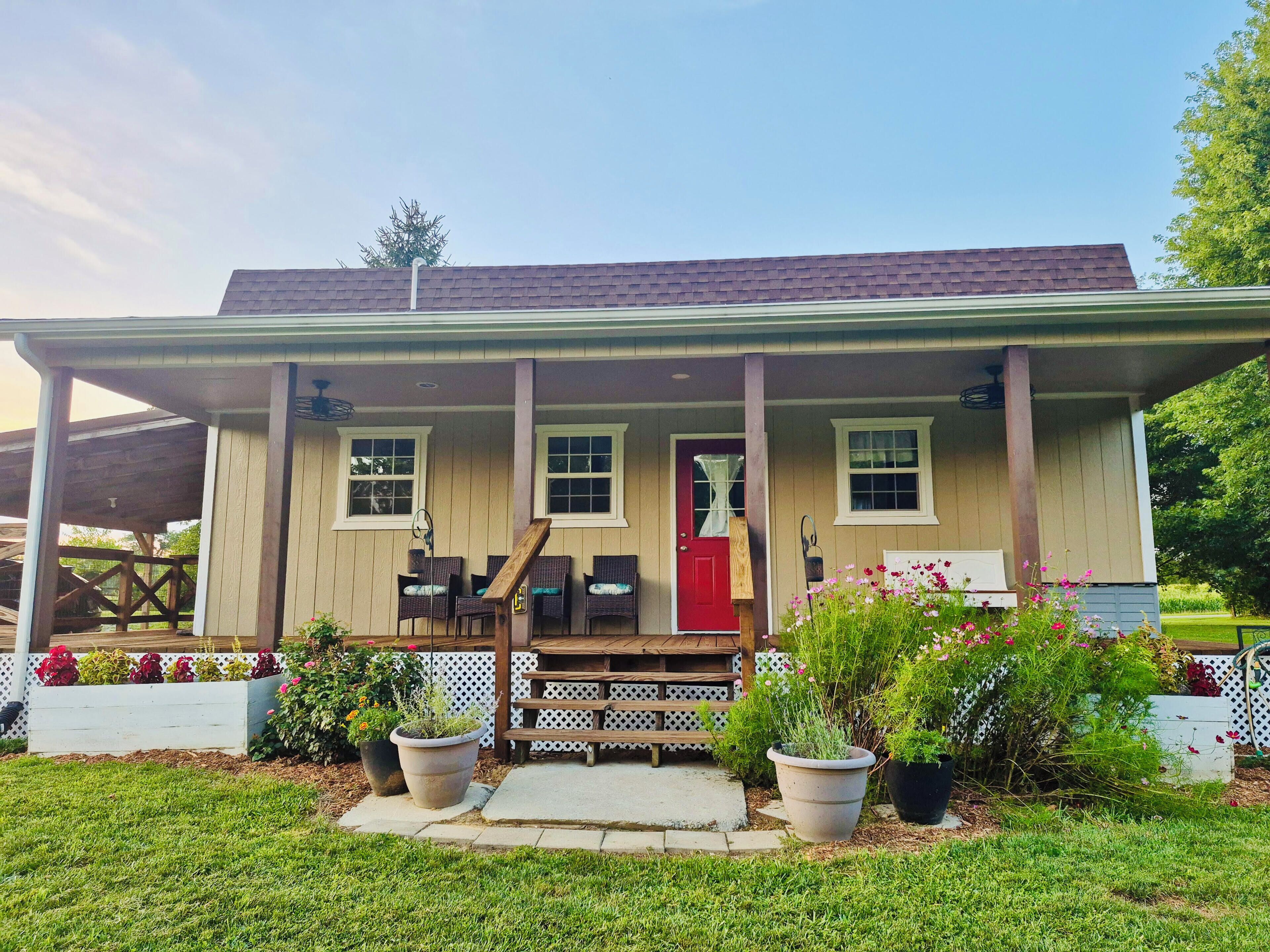 A two-story house with a porch, a red door, and potted plants.