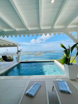 A pool area with a view of the sea, a hanging chair, and a lounge chair with a towel. - Villa Baie des Lucioles—Panoramic View—Heated Pool—Peace and Quiet in Le Marin (Le Marin)