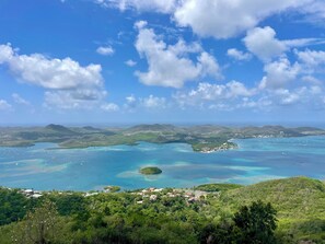 Eine Küstenlandschaft mit blauem Himmel, einer Bucht mit Booten und einer kleinen Siedlung mit Häusern.