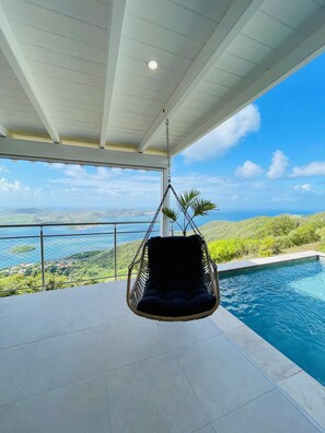 Ein Hängekorbstuhl neben einem Pool mit Blick auf eine gebirgige Landschaft.