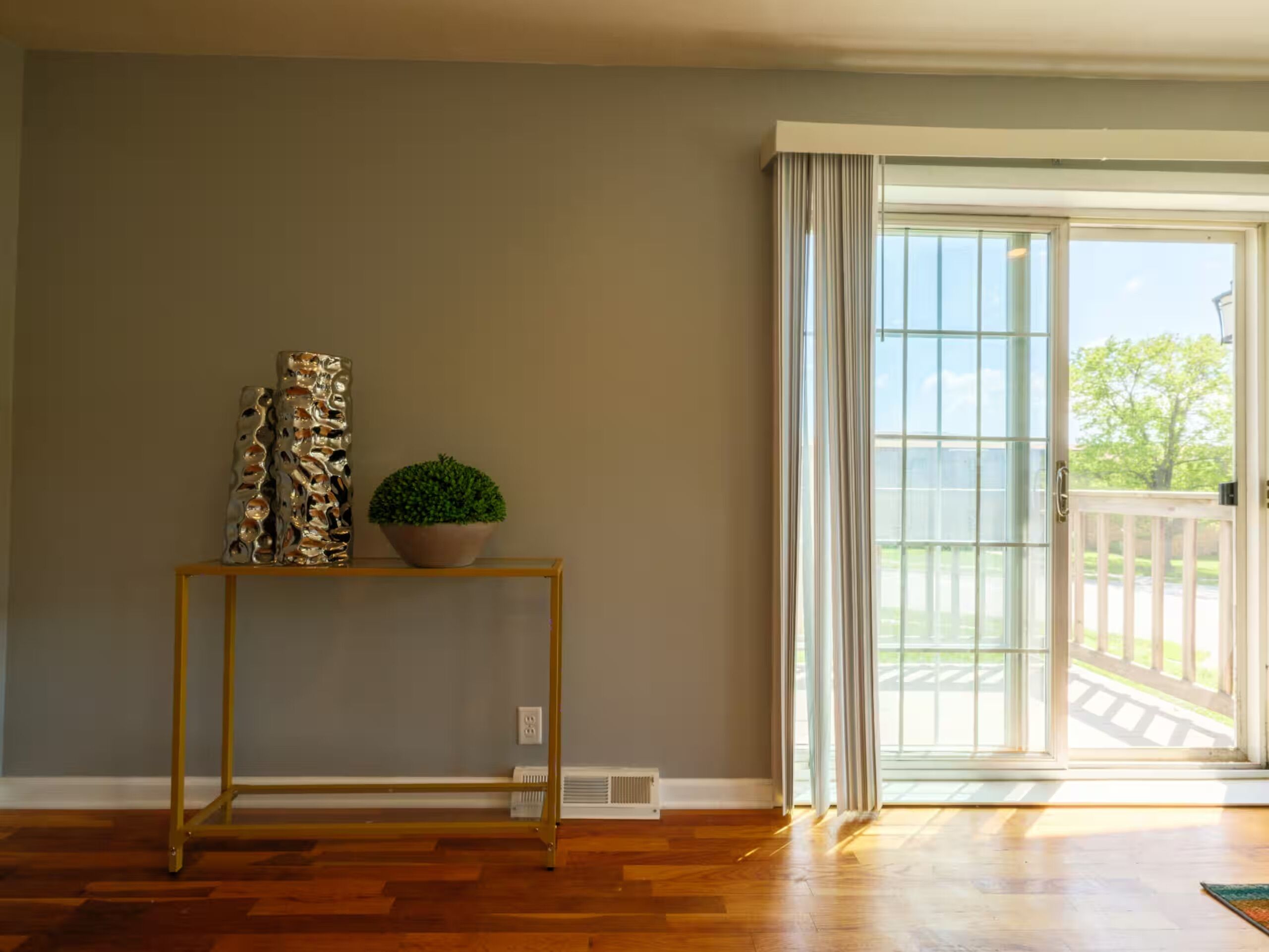 Ein Zimmer mit Holzboden, einem kleinen Tisch mit Pflanze und Dekoration sowie einer Glastür zum Außenbereich.