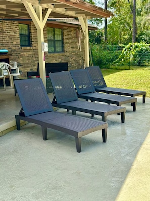 Drei Outdoor-Loungestühle mit Metallgeflecht im Rücken und Holzsitzen, platziert auf einer Betonterrasse vor einem Backsteinhaus.