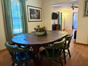 A dining area with a round table, green chairs, a flower vase, and a framed picture on the wall.
