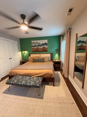 A bedroom with a bed, a nightstand, a lamp, a ceiling fan, a window with curtains, and a mirror. - Dog-Friendly Mountain Home w/ Hot Tub & Rec Room (Asheville)