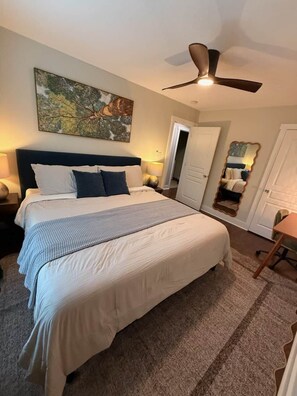 A bedroom with a large bed, a ceiling fan, a painting on the wall, and a door leading to another room. - Dog-Friendly Mountain Home w/ Hot Tub & Rec Room (Asheville)