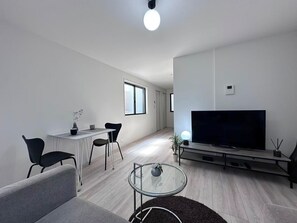 A modern living room with a flat-screen TV, a glass coffee table, and a dining area with chairs.