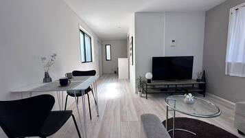 A modern living room with a flat-screen TV, a dining area with a table and chairs, and a sofa.
