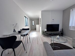 A modern living room with a flat-screen TV, a dining area with a table and chairs, and a sofa.
