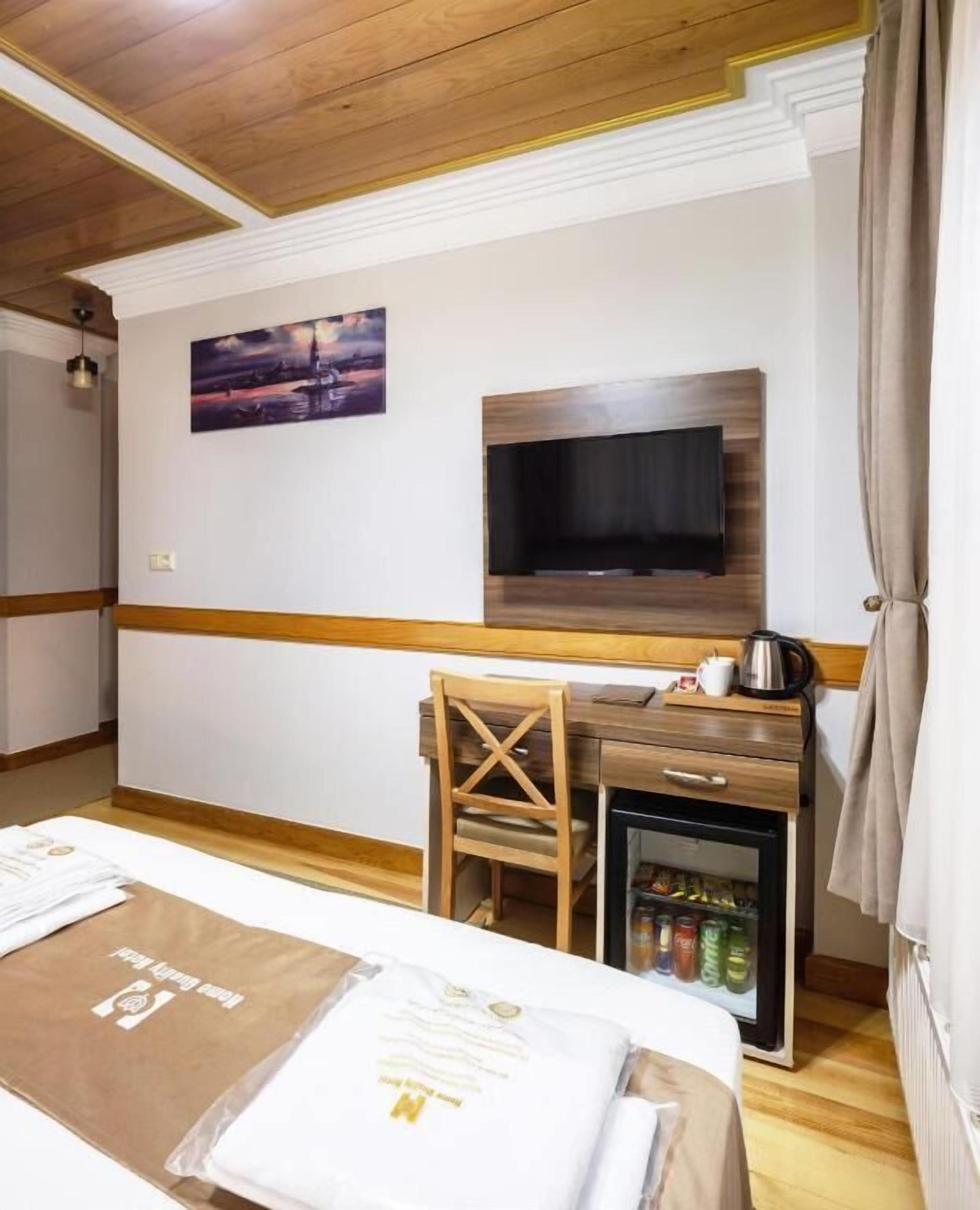 Une chambre d’hôtel comprenant un lit, un téléviseur fixé au mur, un petit bureau avec une bouilloire, un réfrigérateur et une chaise.