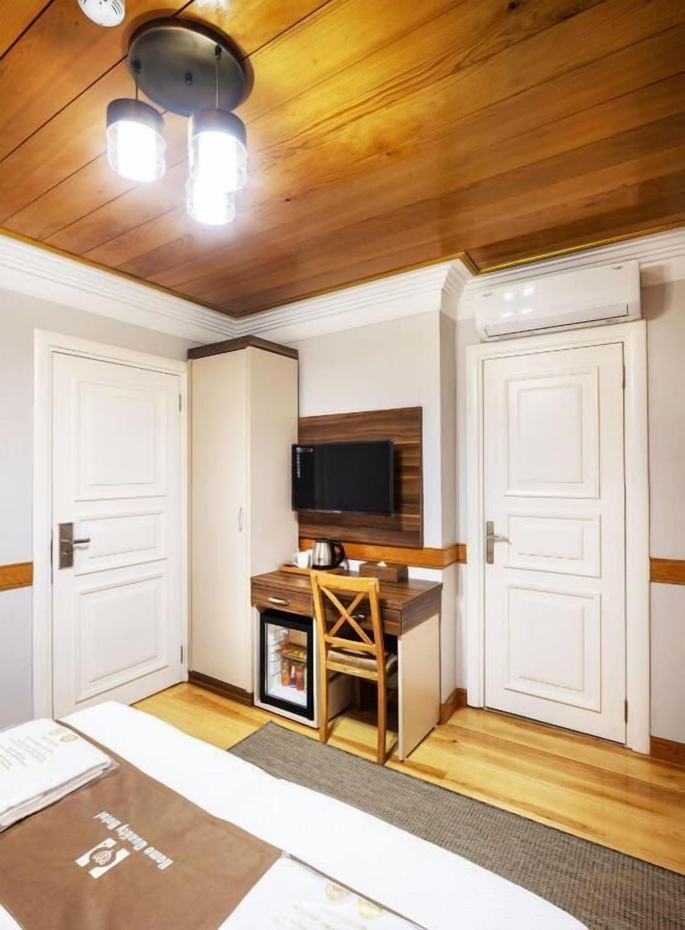 A hotel room with a wooden ceiling, a television, a small table with a chair, and a minibar.