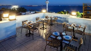 An outdoor dining area with tables and chairs, overlooking a body of water and a distant cityscape. - Home Quality Hotel (Istanbul)