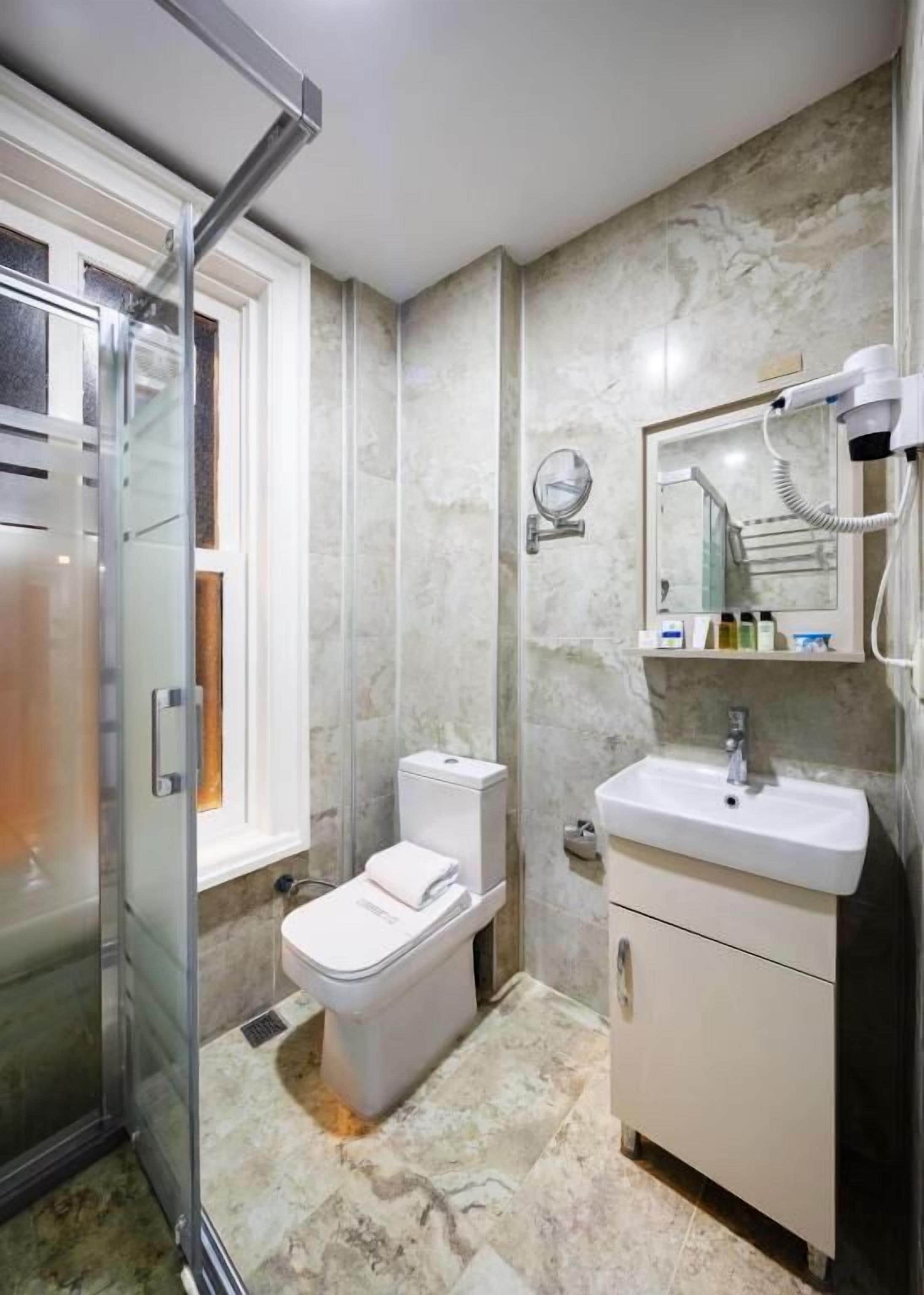 A bathroom with a glass shower enclosure, a toilet, a sink, and a mirror with a hairdryer.
