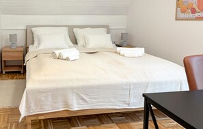 A neatly made bed with white linens, a wooden nightstand with a lamp, and a small table with a chair. - Amazing home in Novi Marof - Kljuc with sauna (Novi Marof - Kljuc)