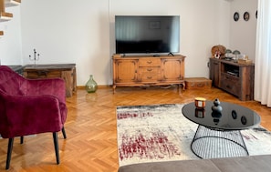 Een woonkamer met een flatscreen televisie, houten meubels, een rode stoel en een salontafel.