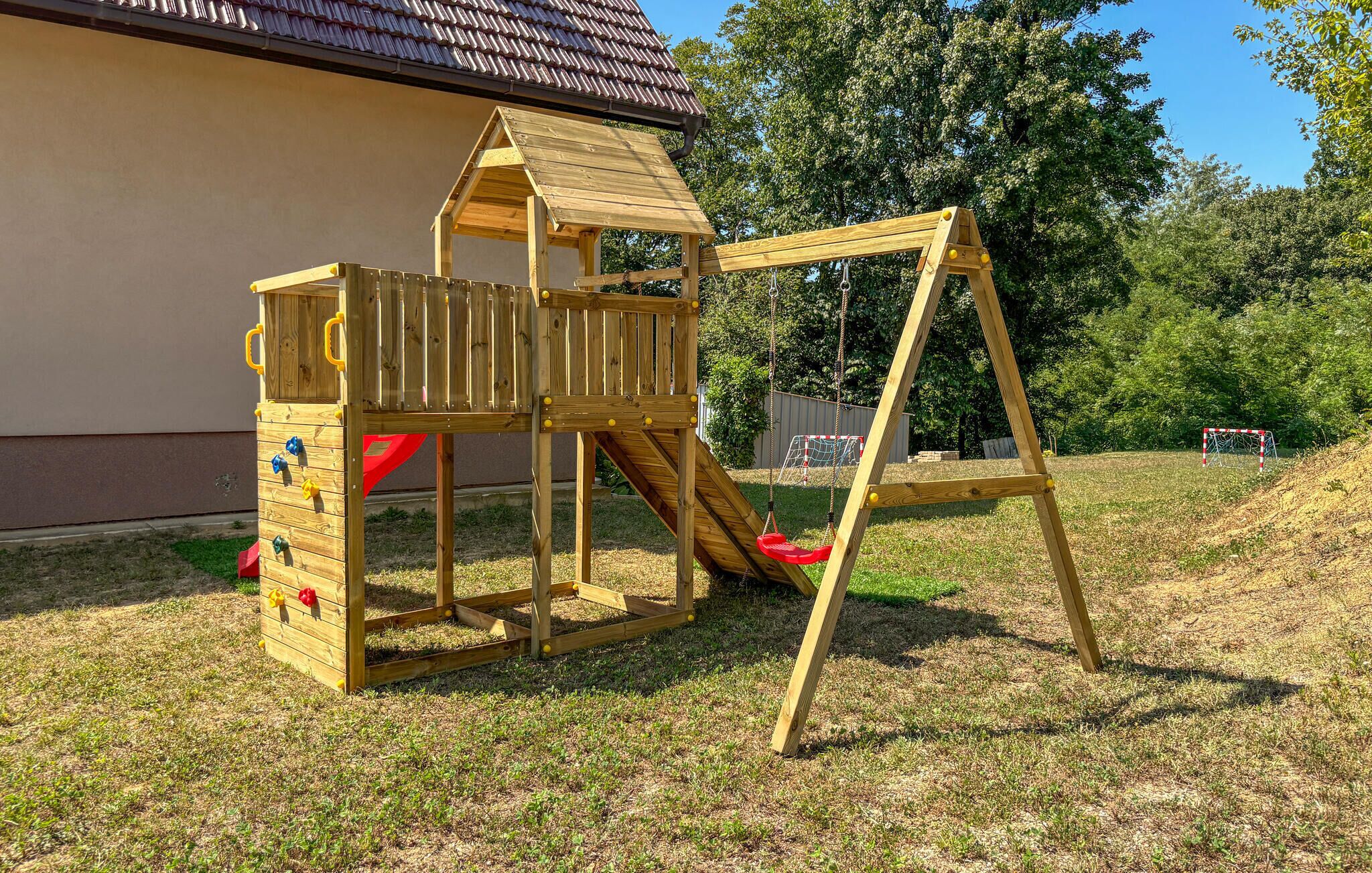 A wooden play structure with a slide and climbing area, set on a grassy lawn.