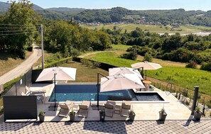 A poolside area with lounge chairs and umbrellas, overlooking a scenic landscape with hills and a village. - Amazing home in Novi Marof - Kljuc with sauna (Novi Marof - Kljuc)
