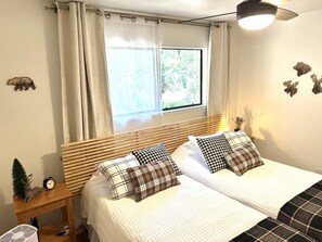 Ein Schlafzimmer mit zwei Betten, einem Fenster mit Vorhängen, einem Nachttisch mit einer Uhr und Wanddekorationen.