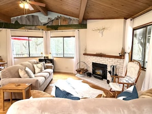 Ein gemütliches Wohnzimmer mit Kamin, einer Couch, einem Sessel und einem großen Fenster.