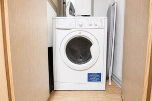 A white washing machine in a laundry room with a blue label. - Stylish Flat • City Centre • Balcony • FreeParking (Milton Keynes)