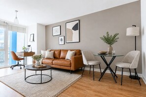 A modern living room with a leather sofa, a round coffee table, and a dining area with a glass table and chairs. - Stylish Flat • City Centre • Balcony • FreeParking (Milton Keynes)
