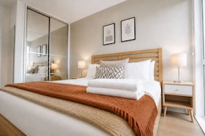 A hotel room with a large bed, a wooden headboard, two bedside tables with lamps, and a large window. - Stylish Flat • City Centre • Balcony • FreeParking (Milton Keynes)